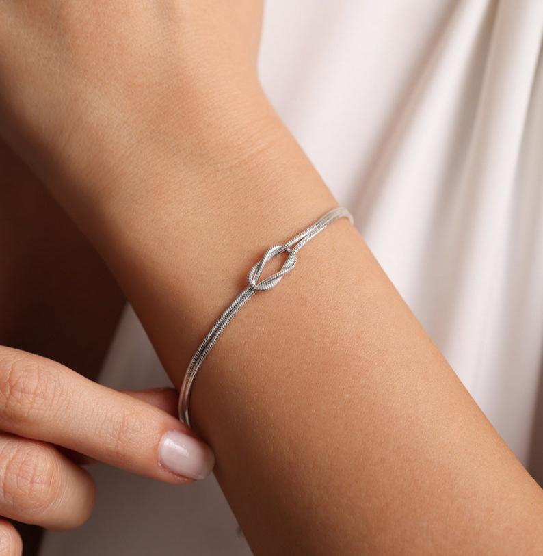 a hand in front of a white t-shirt showing a love knot bracelet for couples